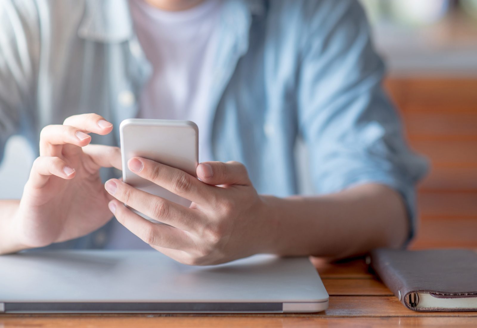 male hand texting message on social media application on smartphone in workspace. Modern lifestyle and digital device concepts